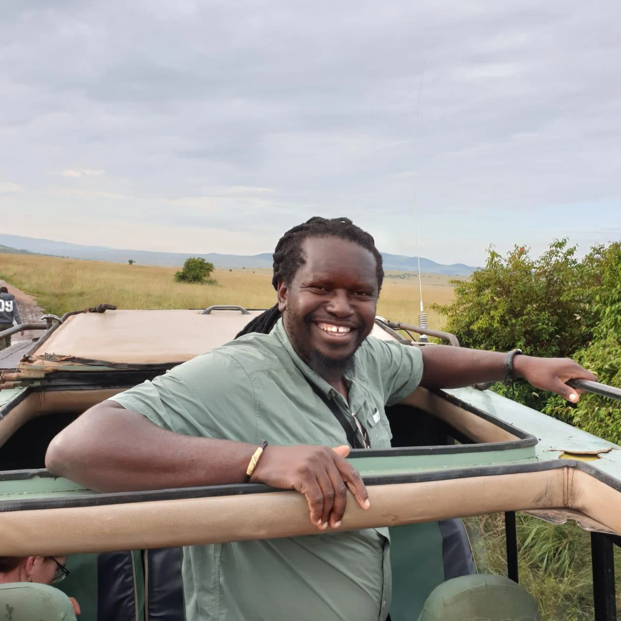 Doctor Mukote leaning out of the open roof of a safari vehicle in the Maasai Mara, Kenya
